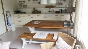A modern kitchen with white cabinets, a wooden dining table, and a bench. - Lovely Bungalow With Garden (Breskens)