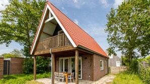 Une maison de plain-pied avec un toit en pente, un balcon et un patio aménagé avec une table et des chaises.