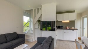 Un salon moderne avec un canapé gris, une table basse blanche et un escalier menant à un espace cuisine doté de meubles blancs et d’un téléviseur à écran plat.