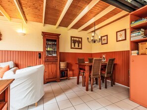 Uma área de refeições com uma mesa e cadeiras de madeira, um armário com portas de vidro e uma estante.