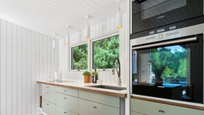 Una cocina moderna con horno empotrado, un fregadero con ventana encima y una planta en maceta sobre la encimera.
