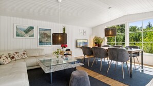 Una sala de estar moderna con una mesa de centro de vidrio, un sofá gris y un comedor con una mesa y sillas de madera.