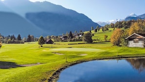 Um campo de golfe tranquilo com lago, casas e montanhas ao fundo.