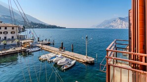 A marina with boats docked, a pier extending into the water, and a building with a balcony overlooking the scene. - Lovely apartment for 3 guests with A/C, WIFI, TV, patio, pets allowed and panoramic view (Malcesine)