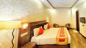 Une chambre d’hôtel avec un grand lit, une tête de lit en bois, un bureau, deux chaises, une télévision et un ventilateur de plafond.