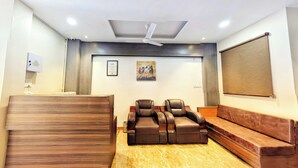 Un espace d’accueil comprenant un comptoir de réception en bois, deux fauteuils inclinables en cuir, un canapé marron, un ventilateur de plafond et un certificat encadré accroché au mur.