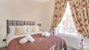 A hotel room with a large bed, floral curtains, and a view of buildings outside. - The Walmgate Retreat

 (York)