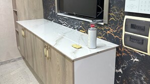 Et moderne køkken med marmor bordplade, træskabe, indbygget fjernsyn og et panel til styring på væggen.