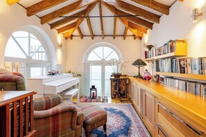 Un rincón acogedor para leer con un piano, sillones cómodos, una estantería y un ventanal grande.