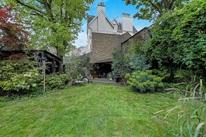 A residential backyard with a stone wall, a wooden deck, and various plants.