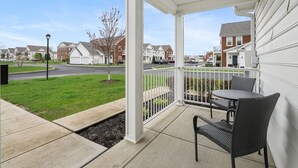 Un espace extérieur abrité, avec une table et des chaises, donnant sur une rue résidentielle, et agrémenté d’un petit arbre.