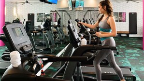 Une salle de sport équipée de plusieurs tapis de course, où une femme s’entraîne sur l’un d’eux, ainsi que divers appareils d’exercice.