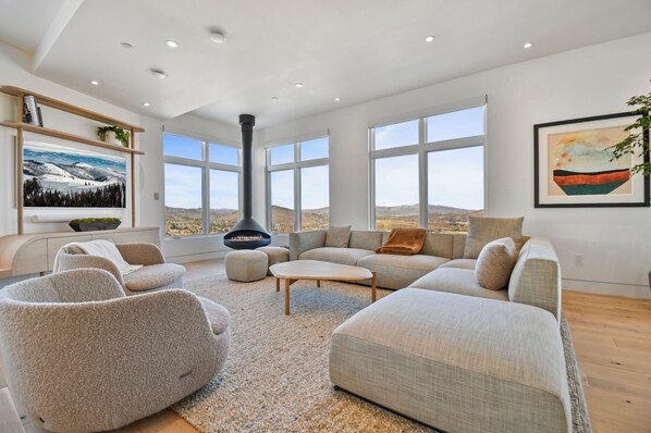 A spacious living room with a fireplace, large windows, and a view of the countryside.