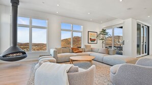 Ein geräumiges Wohnzimmer mit großem Kamin, einer Sofagarnitur und Blick auf die Landschaft durch große Fenster.