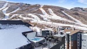 Ein Hotel mit Pool auf dem Dach, Skipisten im Hintergrund und einer Berglandschaft.