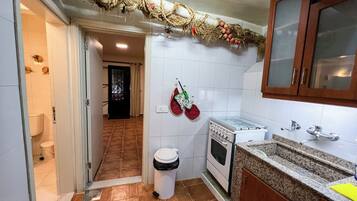 A compact kitchen with a gas stove, a trash bin, and a sink.