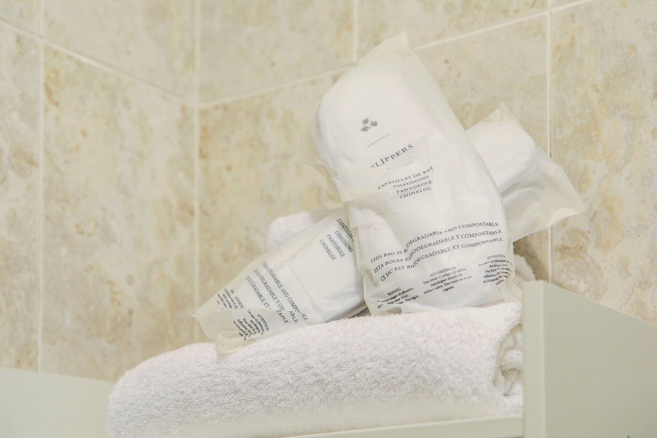 Une salle de bain avec une serviette blanche et un sac de chaussons.