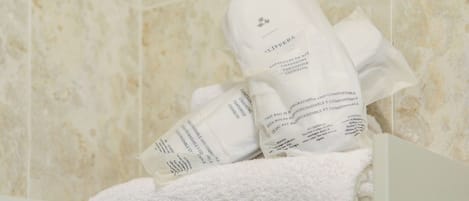 Une salle de bain avec une serviette blanche et un sac de chaussons.