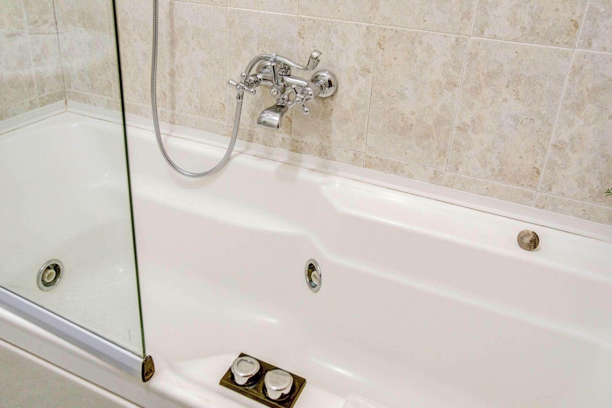 A white bathtub with a chrome showerhead and faucet, set against a tiled wall.