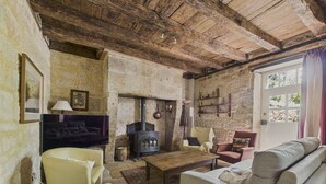 A rustic living room with stone walls, a wooden ceiling, a fireplace, a sofa, a television, and a coffee table. - Salignac-Eyvigues, house for 7 with pool (Salignac-Eyvigues)