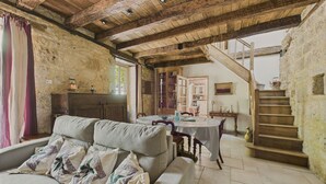 A rustic interior with a wooden ceiling, stone walls, a sofa with patterned cushions, a dining table, and a staircase leading to an upper level. - Salignac-Eyvigues, house for 7 with pool (Salignac-Eyvigues)