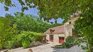 A stone building with a red door, surrounded by lush greenery and a gravel path. - Salignac-Eyvigues, house for 7 with pool (Salignac-Eyvigues)