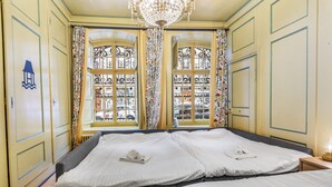 Une chambre d’hôtel avec deux lits, un lustre et de grandes fenêtres ornées de ferronnerie.
