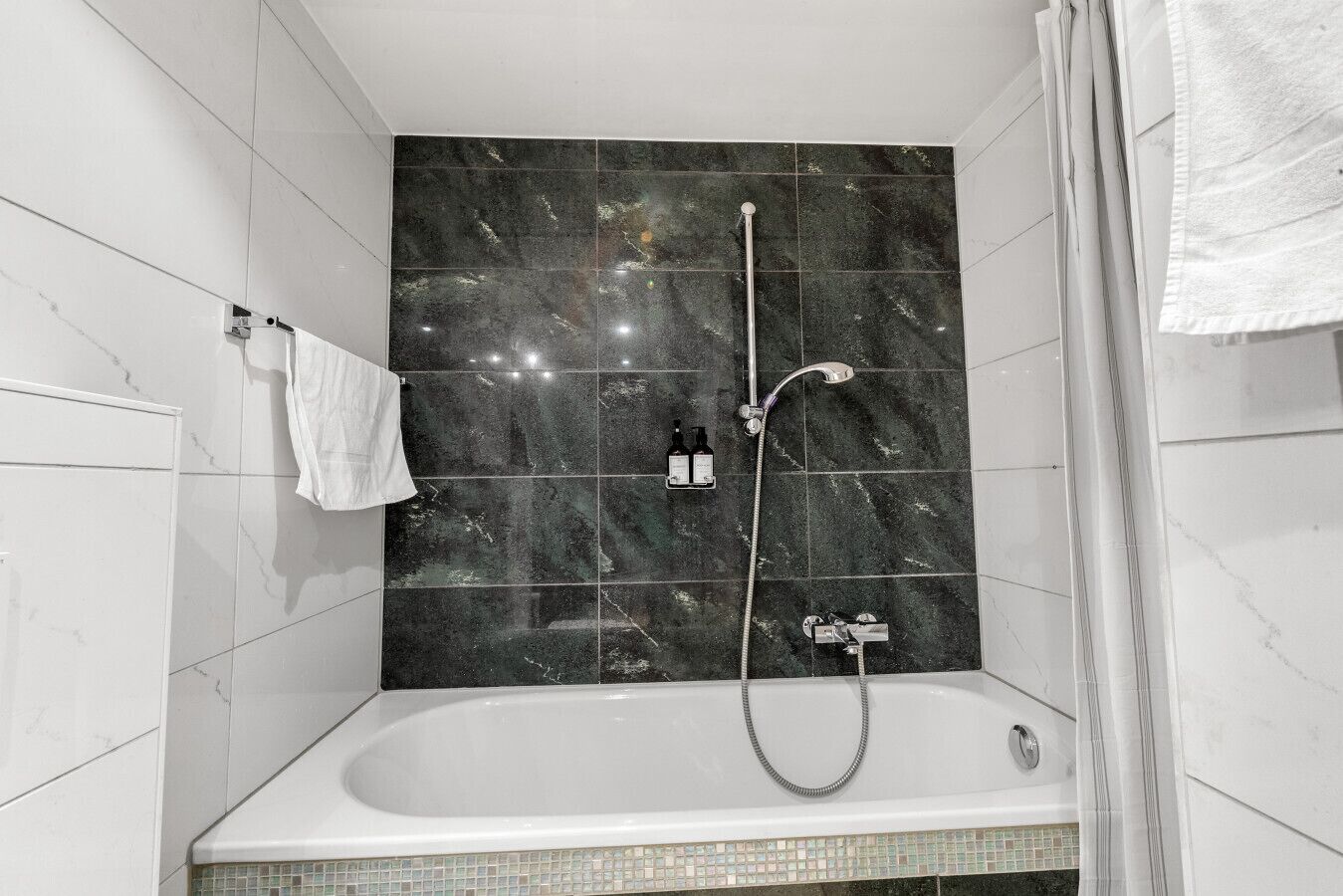 Une salle de bain avec une baignoire, une douche et un mur recouvert de carreaux.