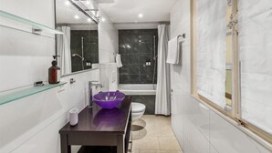 Une salle de bain moderne avec une étagère en verre, un lavabo violet, des toilettes et un espace douche.