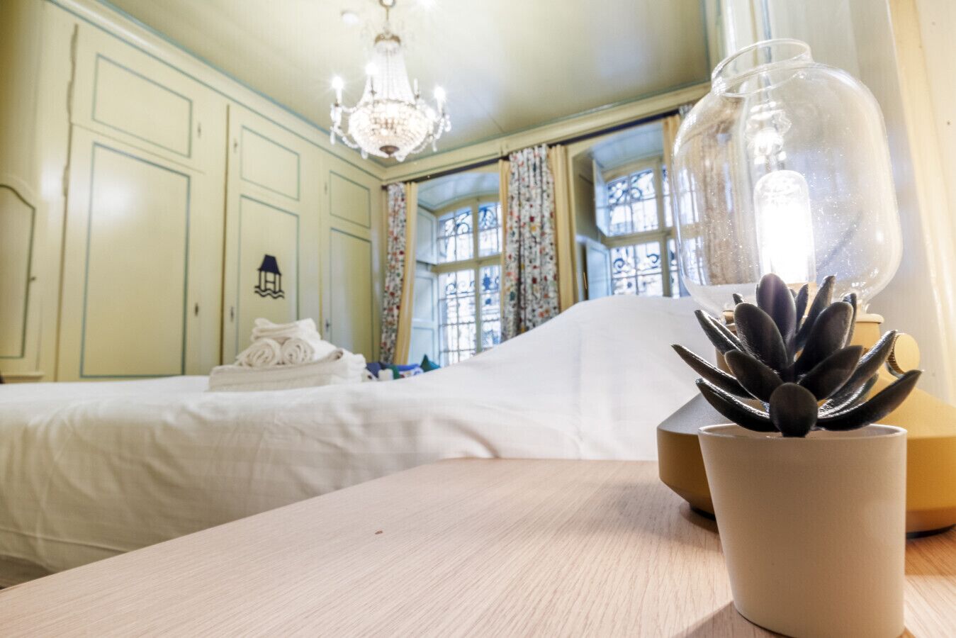 A hotel room with two beds, a chandelier, a potted succulent, and a window with curtains.