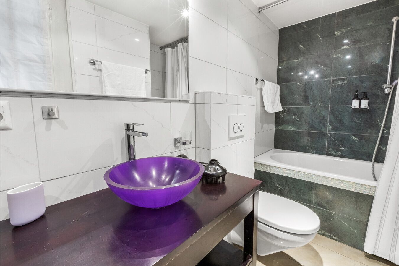 Ein modernes Badezimmer mit einem violetten Waschbecken, einer weißen Toilette und einer Duschkabine.