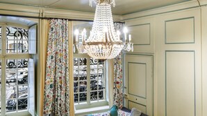 Une pièce avec un lustre, des rideaux à motifs floraux, une fenêtre avec des barreaux et un lit.