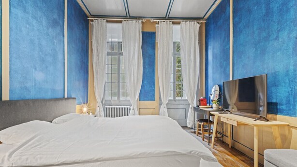 Una habitació d'hotel amb un llit gran, una taula amb televisió i una finestra amb cortines.