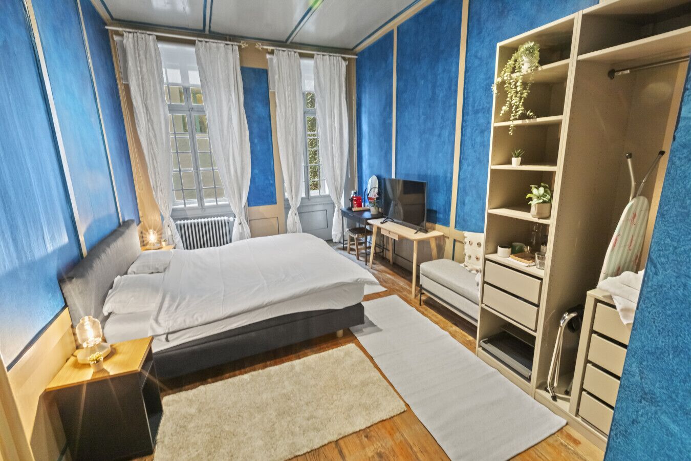 Ein Schlafzimmer mit Bett, Schreibtisch, Fernseher, Kleiderschrank und Heizkörper.