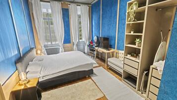 Ein Schlafzimmer mit Bett, Schreibtisch, Fernseher, Kleiderschrank und Heizkörper.