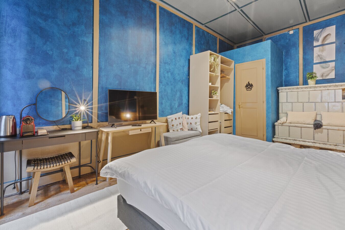A bedroom with a bed, a desk with a computer, a TV, a wardrobe, and a door.