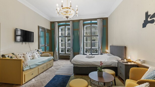 Et hotelværelse med seng, sofa, fjernsyn, lysekrone og udsigt over byen.