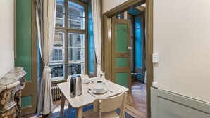 Et lille spiseområde med et bord dækket til to personer, en radiator og et vindue med gardiner.