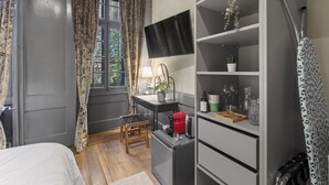 Una camera compatta con un letto, una scrivania, una sedia, una TV e una libreria con diversi oggetti.