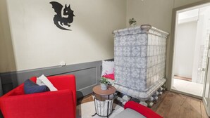 Una stanza con una poltrona rossa, un divano bianco, un pannello decorativo con un drago nero, un caminetto in maiolica e un tavolino con una pianta.
