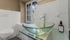 A bathroom with a glass bowl sink, a toilet, and a hand soap dispenser. - Charming studio in Fribourg's old town (Fribourg)
