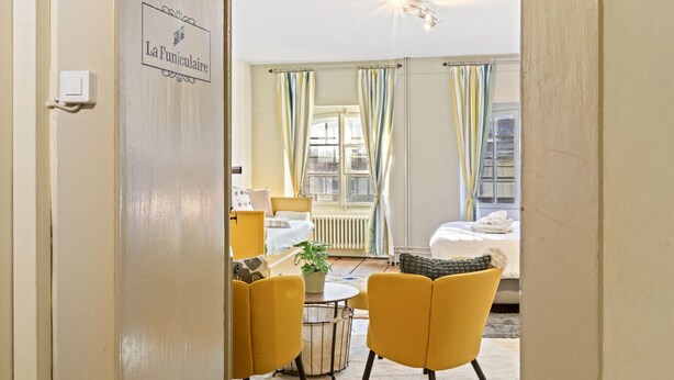 A hotel room with a bed, a yellow armchair, a small table, and a potted plant. - Bright studio in Freiburg's old town (Fribourg)