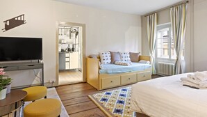 A hotel room with a bed, a desk with a TV, a sofa, and a small dining area with yellow chairs. - Bright studio in Freiburg's old town (Fribourg)