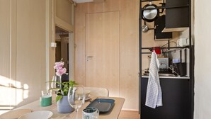 A dining area with a wooden table set for two, a potted plant, and a kitchen area with a black cabinet and a hanging towel. - Bright studio in Freiburg's old town (Fribourg)