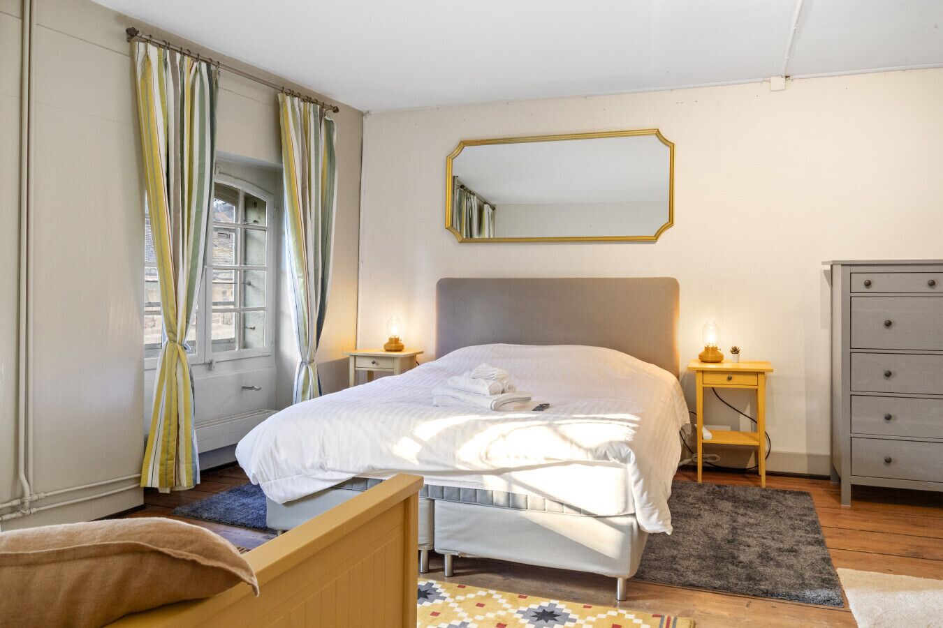 Ein Schlafzimmer mit Bett, Nachttischen, einem Schminktisch, einem Spiegel und einem Fenster mit Vorhängen.