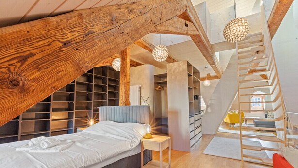 Une chambre avec un espace nuit en mezzanine, des étagères intégrées et un escalier en bois.