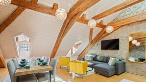 Un espace de vie de style loft avec des poutres en bois apparentes, un coin repas comprenant une table et des chaises en bois, un canapé et des suspensions sphériques.