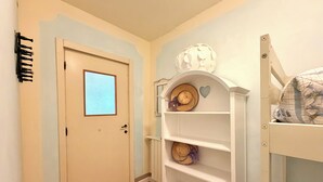 Un corridoio con una porta bianca, uno scaffale con cappelli e un letto a castello.