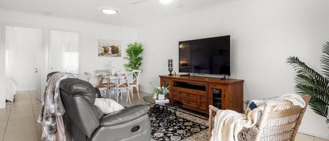 A modern living room with a leather sofa, a wicker chair, a TV on a wooden cabinet, and a patterned rug.