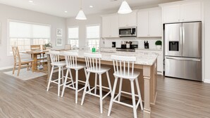 Une cuisine moderne avec des meubles blancs, des appareils en acier inoxydable et un îlot central doté de tabourets de bar.